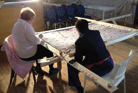 Two women sitting at a table working on a quilt 