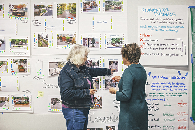 Two woman look at a wall covered with photos and ideas involving the redesign of a town's Main Street