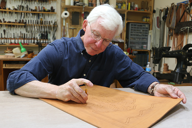 An older man carves a piece of leather