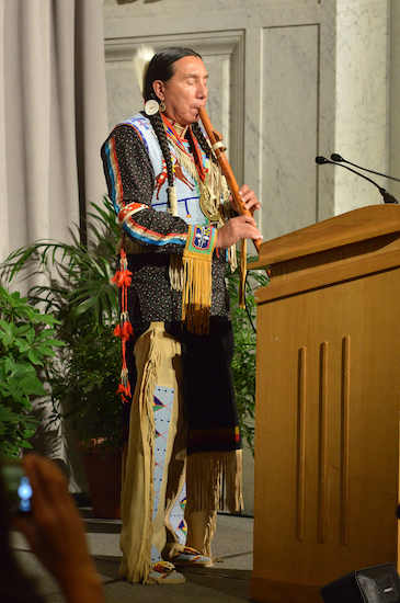 Heritage Fellow in traditional Dakota dress playing the flute