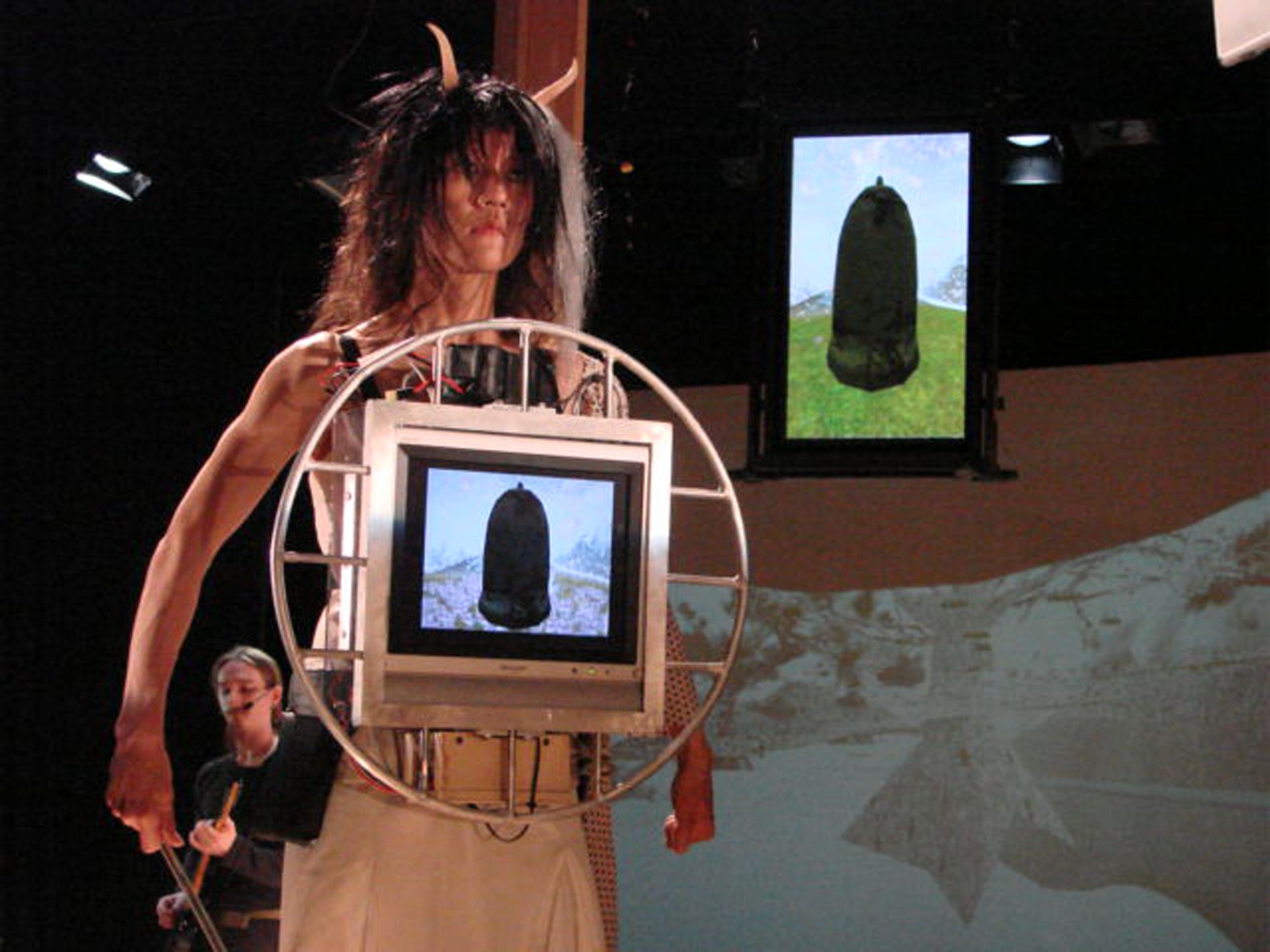 Woman with horns and a computer monitor connected to her chest. 