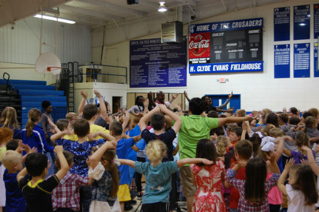Dancers lead an assembly of schoolchildren in a school gym