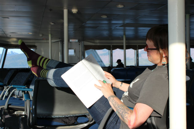 A lady reading a book with her feet up on a ferry