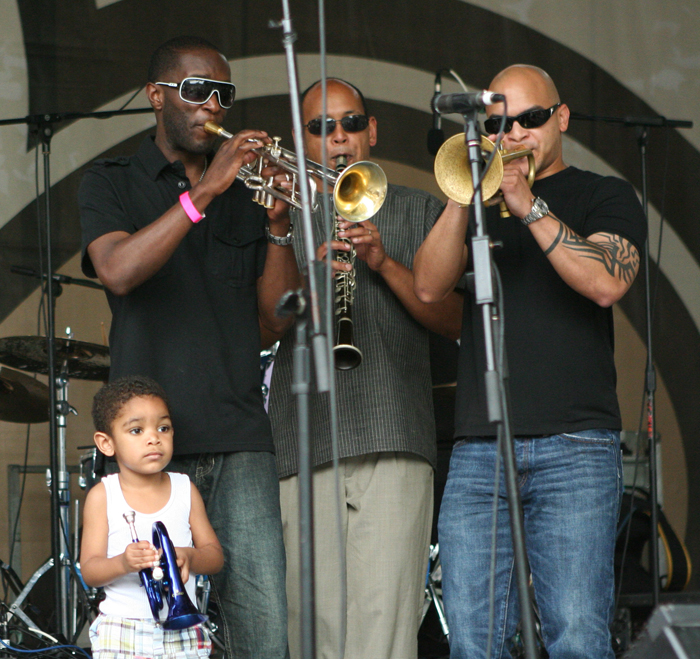 Three men and a boy performing on horns. 
