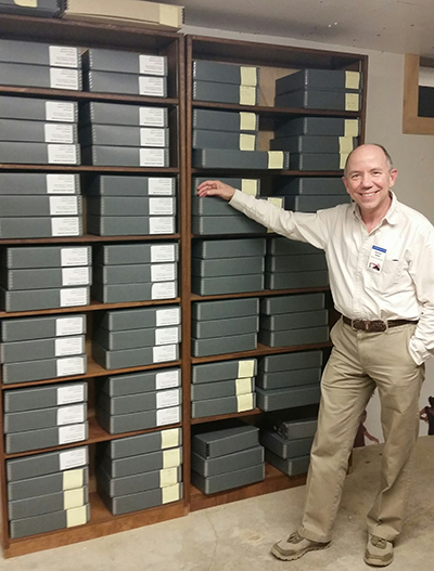 Man standing in front of bookcases full of photo boxes. 