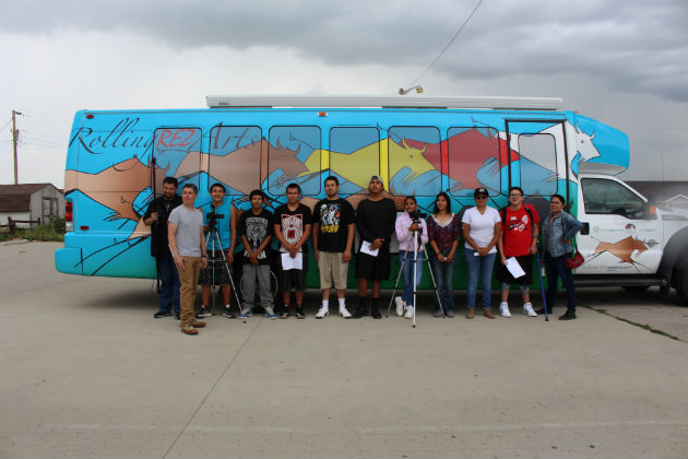 Teens and adults with film equipment stand in front of a blue bus with buffalo painted on it