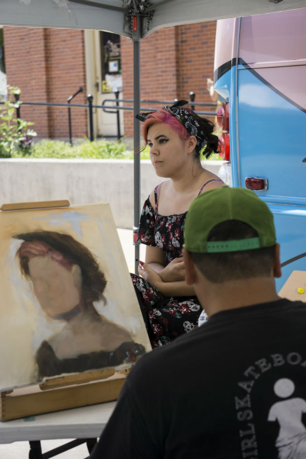 A man paints a portrait of a woman with pink hair