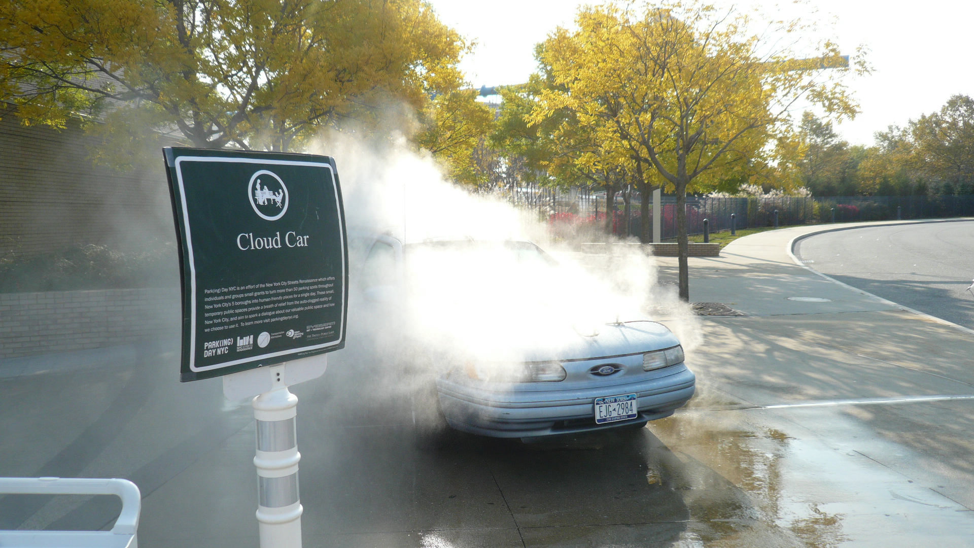 Smoking pouring out of a car behind a sign. 