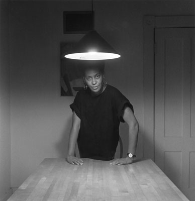 photograph of a black woman standing behind a bare kitchen table