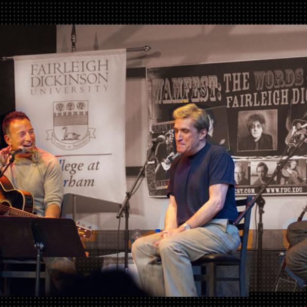 Musician Bruce Springsteen laughs as he reacts to poet Robert Pinsky and author Wesley Stace on stage at the Words and Music Festival, 2010.  The backdrop is a WAMFEST poster with images of participating artists.