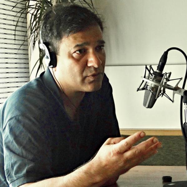 Abbas Raza with headphones and speaking into a microphone.