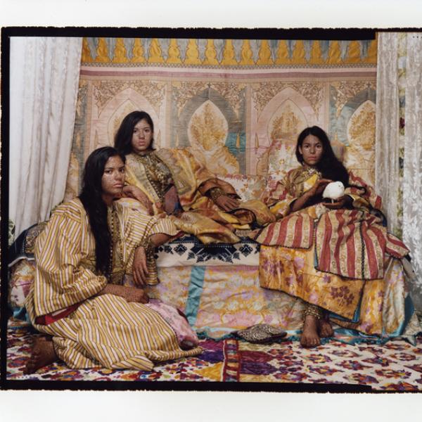 Three women in colorful clothes with hena-colored bodies.
