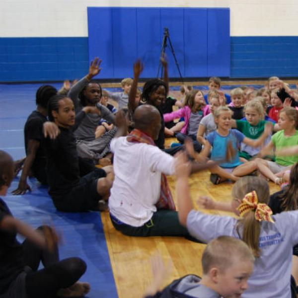 Dancers sit on floor leading a group of young children in movements