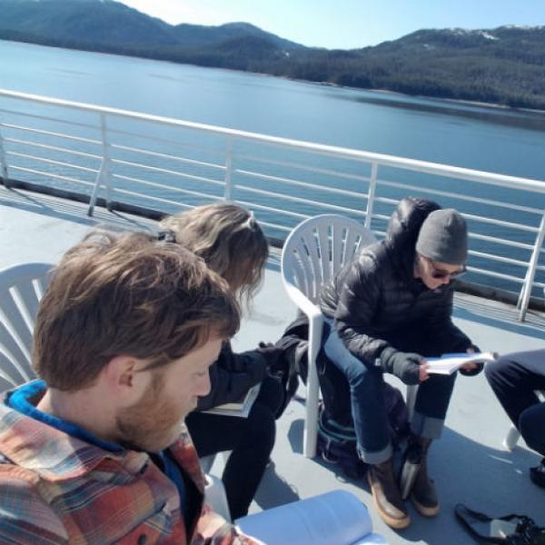 People reading papers sitting on the deck of a ferry in Alaska