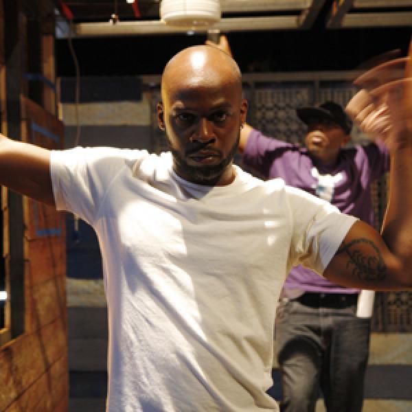African-American man in white tee-shirt in building shaking his arm.