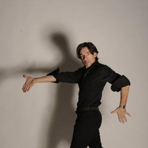 Man dressed in black in a dance pose with arms extended.