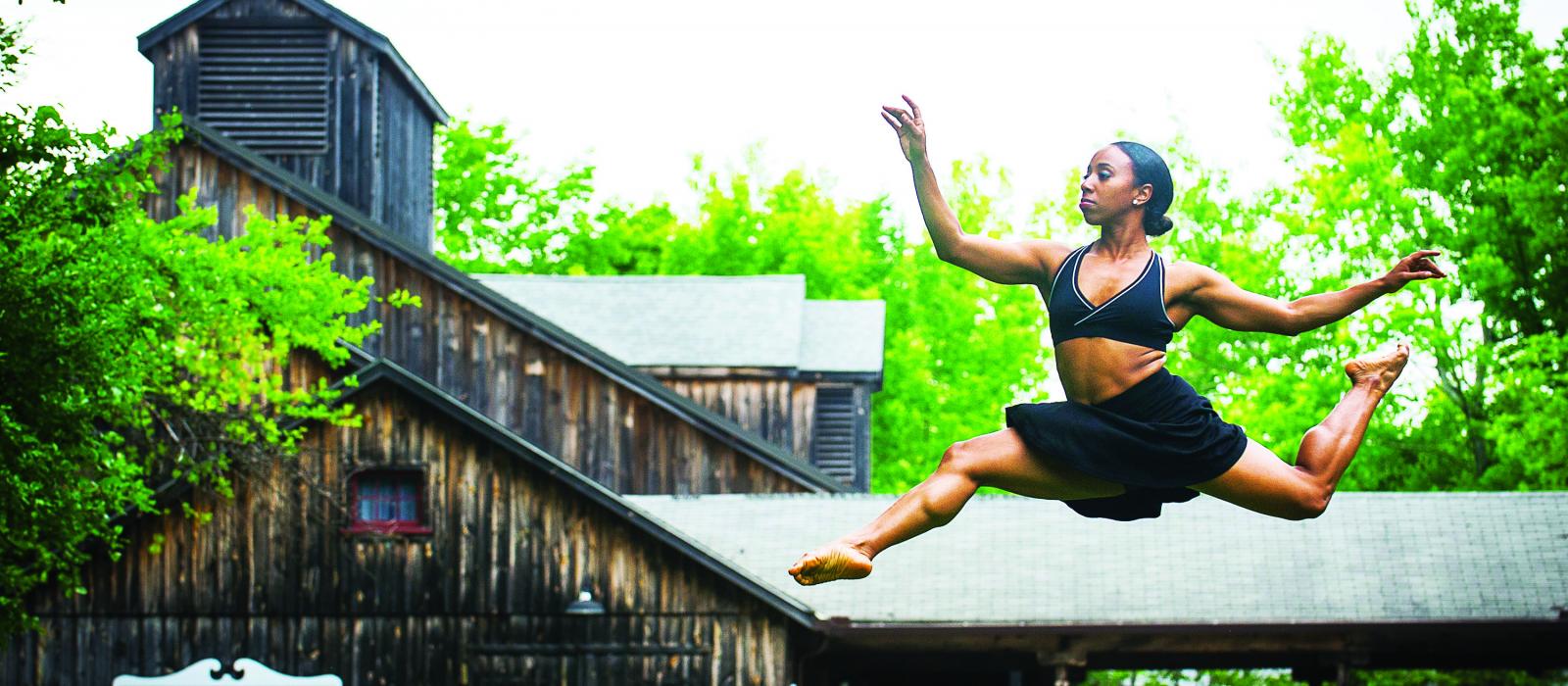 Woman leaping into air in front of barn.