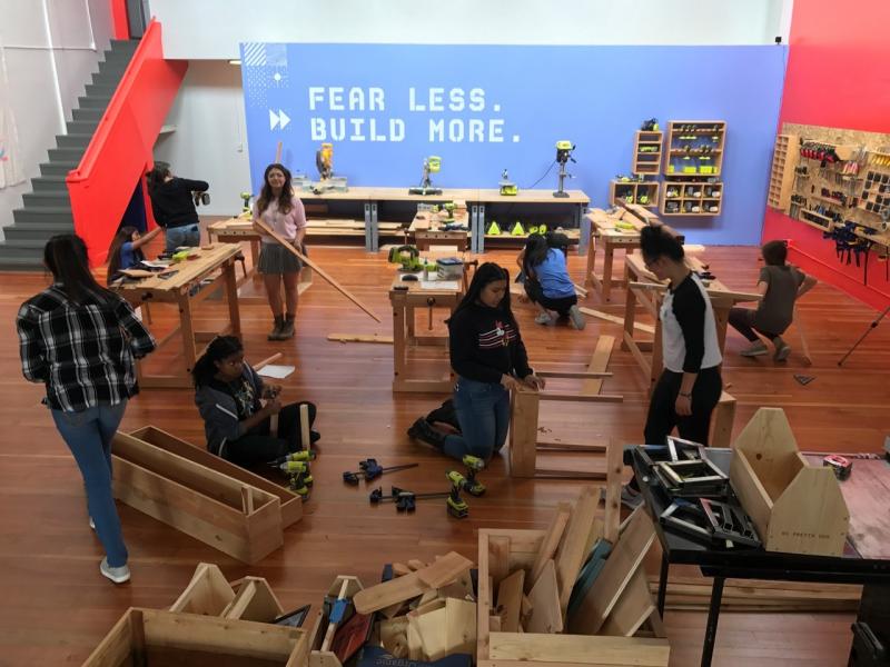 In a large open space, a group of high school girls construct furniture. 