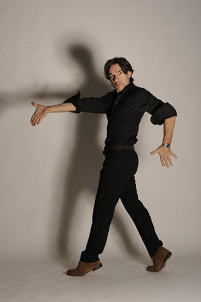 Man dressed in black in a dance pose with arms extended.