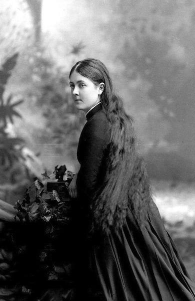 a black and white photo from the early 20th century of a young white woman with long dark hair and Victorian dress