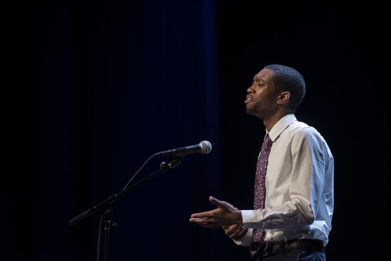 A young Black man recites behind a microphone