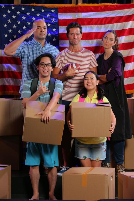 Actors portraying a family hold cardboard boxes while standing in front of an American flag as one salutes