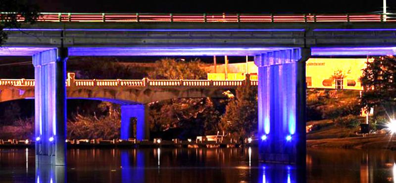 Night shot of a bridge over a river illuminated with purple light