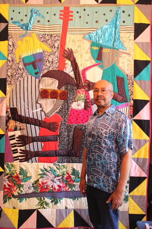 A man stading in front of a large quilt.