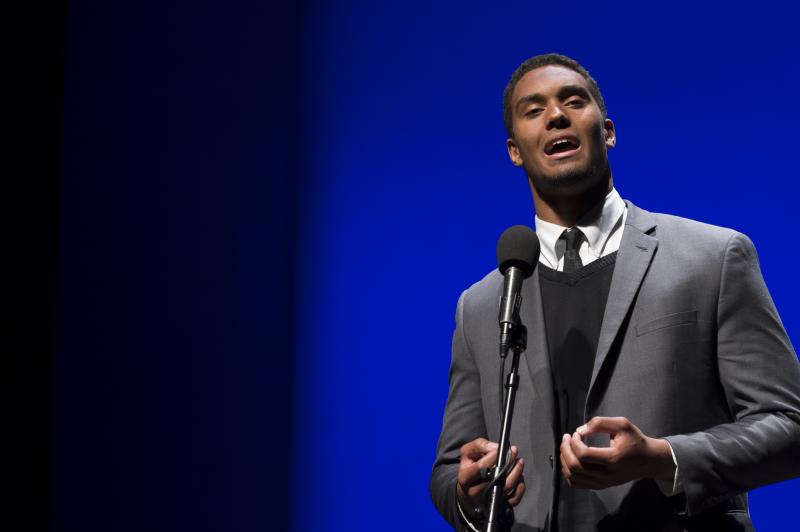 A young Black man recites behind a microphone