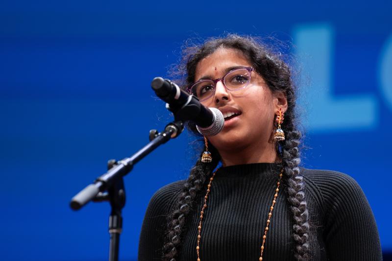A young Indian woman recites poetry behind a microphone