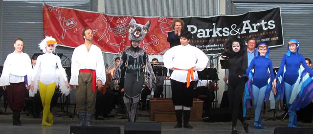 Dancers in a variety of costumes on stange in front of a large Parks and Arts banner