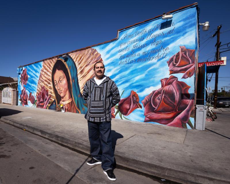 A man poses in front of a mural.