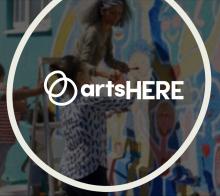 Circle ArtsHERE logo superimposed over a blurred background of people working on an outdoor mural