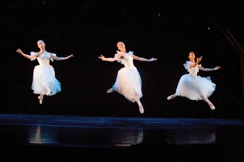 Three women in long white dresses dancing on stage.
