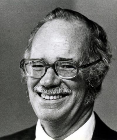 Portrait of balding man wearing large-framed glasses and smiling. 