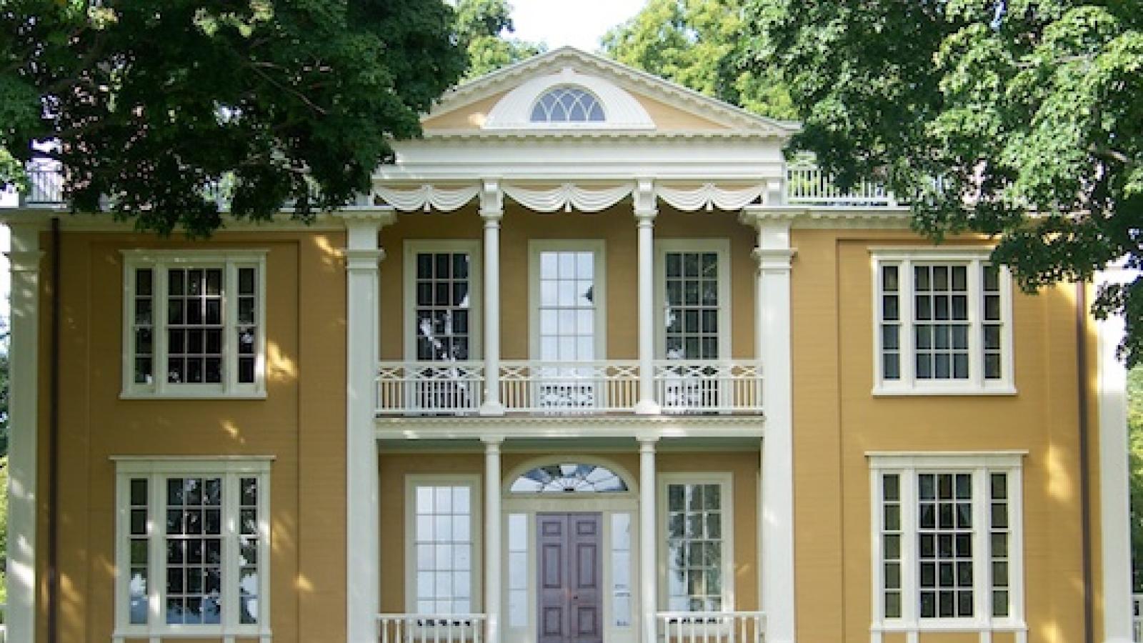 the facade of a yello multi-story Federal-style house with a columned porch and multiple windows
