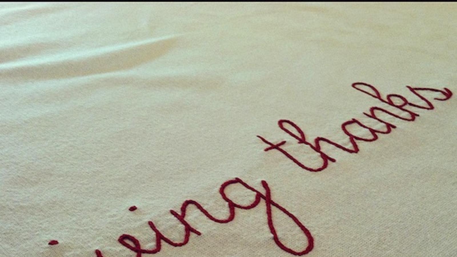The phrase "giving thanks" embroidered in red thread on a white background