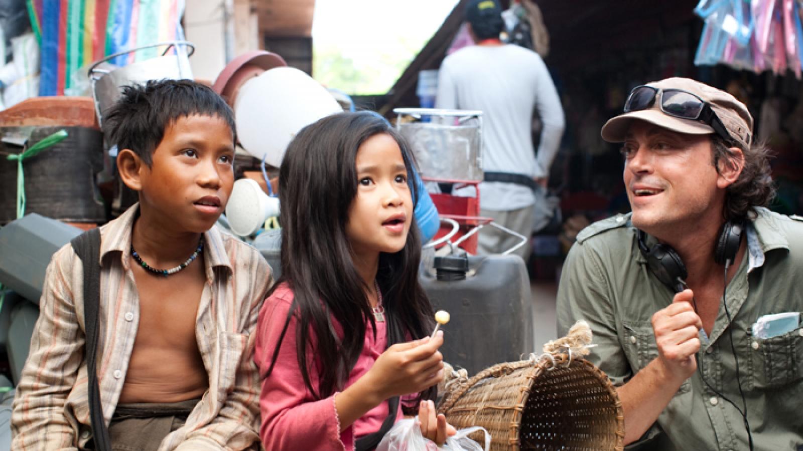 Director wearing hat with two Laotian children. 