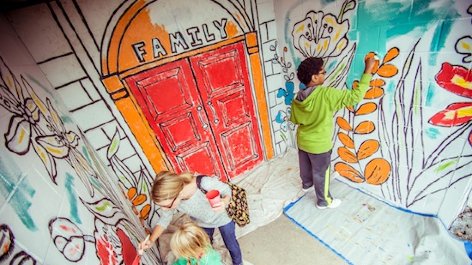 Three people work on filling in the colors on a wall mural