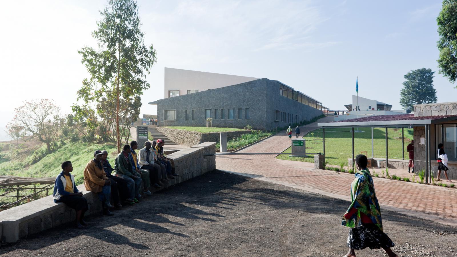 People sit on a stone bench as another walk by outside of a hospital in Rwanda