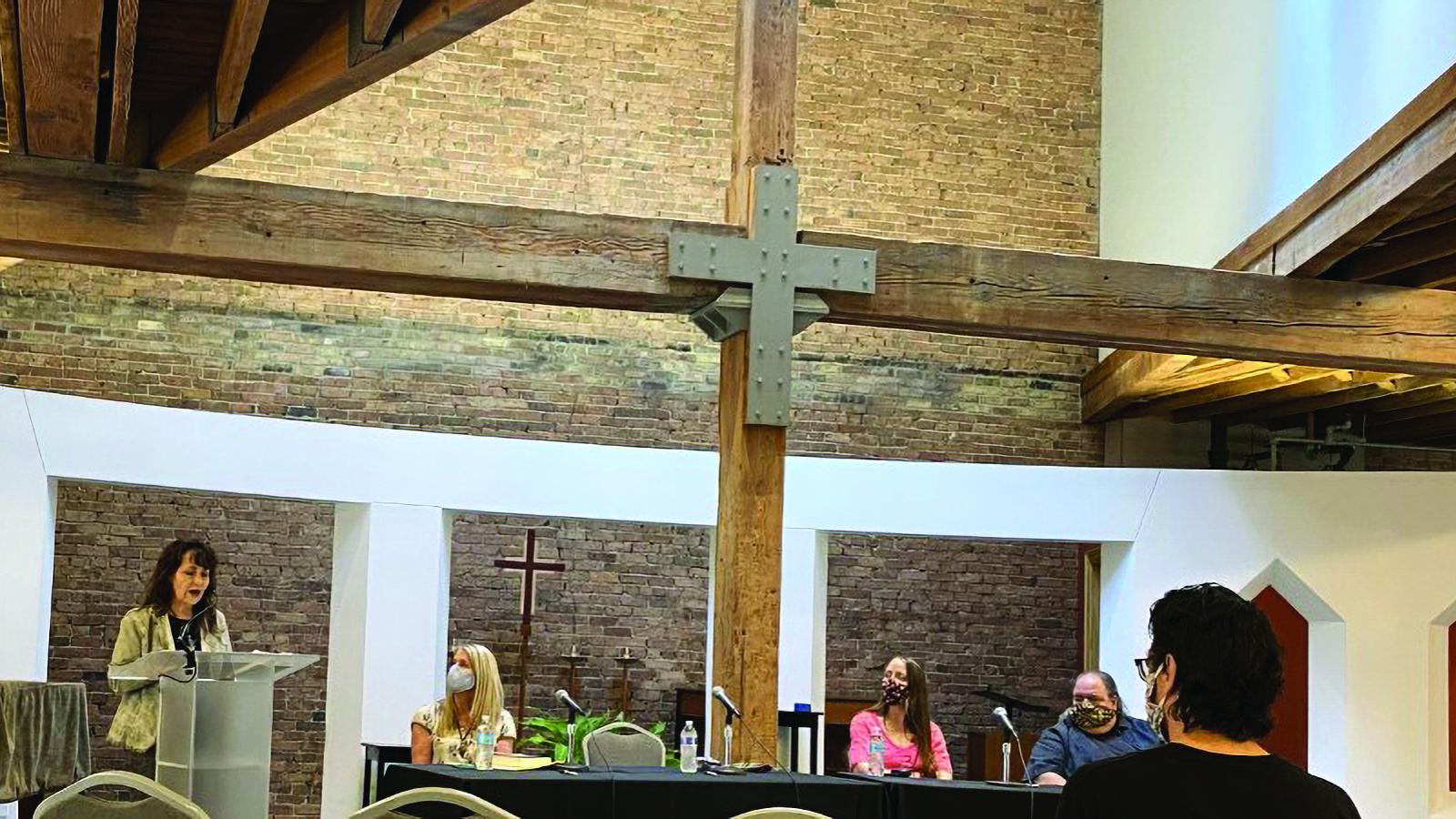 Woman reading from podium in a church with large crucifix showing. 