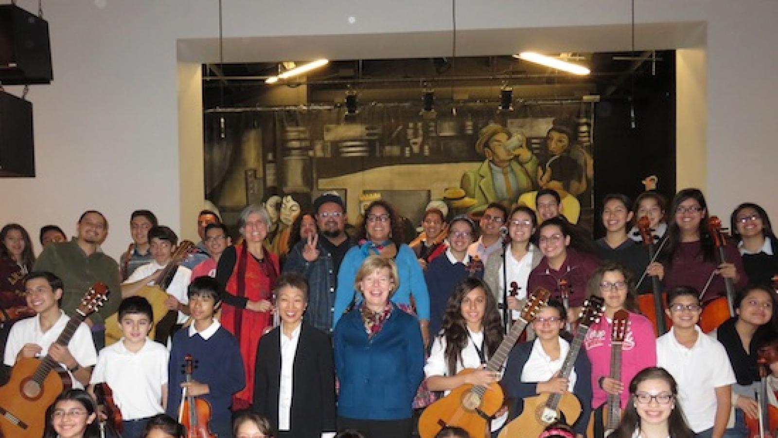 Jane Chu and Senator Tammy Baldwin with a large group of kids holding stringed instruments