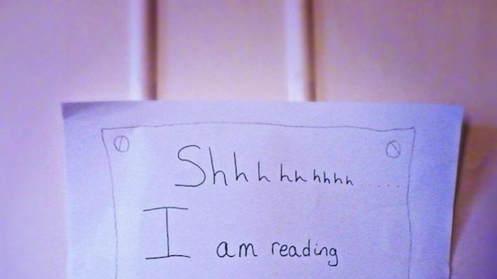 Close-up of a door with stickie note that says "Shhh, I am reading. Please knock. Thank you mum"