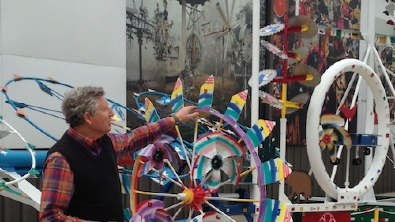 A man shows off a whirligig which is like a looks like a decorated spinning wheel