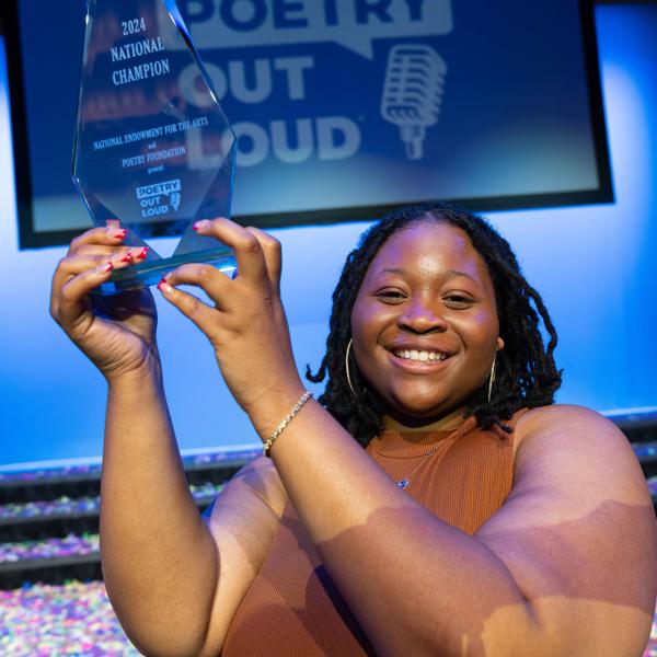 Niveah Glover, a young Black woman, holding her Poetry Out Loud National Champion trophy aloft