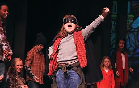 Cast of young actors, with one front and center with arm raised shouting something to the audience