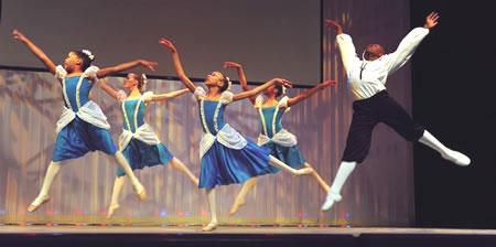 Four women and a man mid-leap on stage in a ballet performance