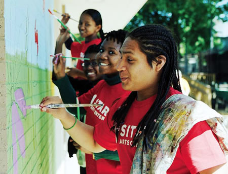 Smiling African American female students working on a mural on a brick wall