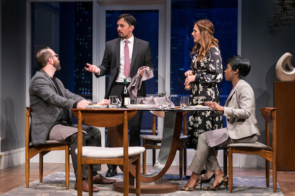 a man and a woman sit at a modern looking dining table while another man and another woman stand near them and all are in conversation