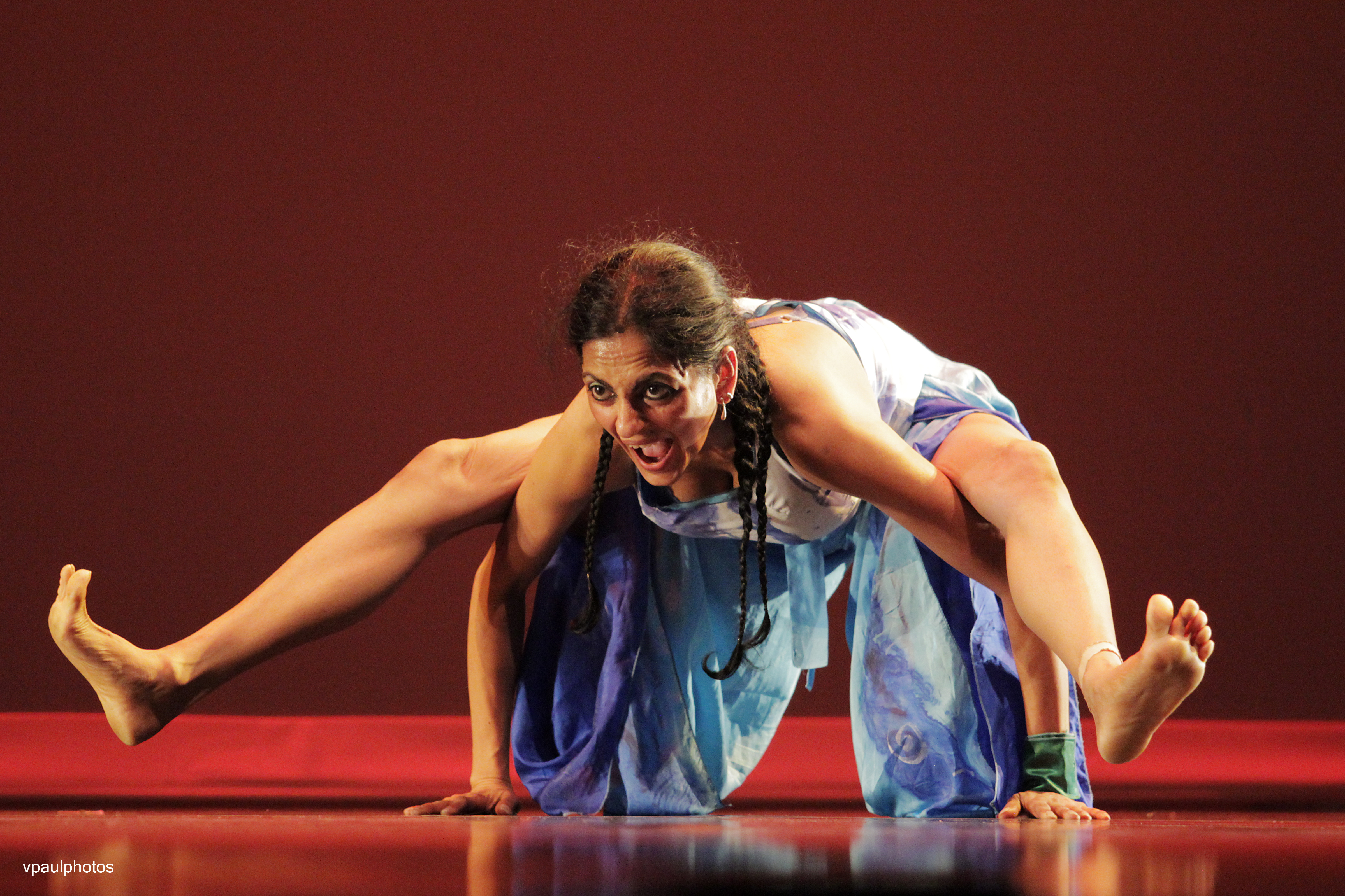 Female dancer, on stage, balancing her body on her hands with a angry face.